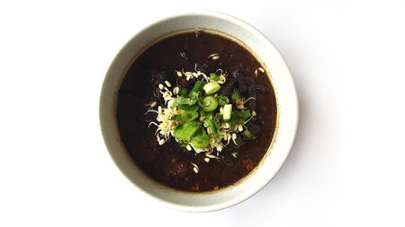 Black meat soup Rawon with leeks and bean sprouts in a white bowl isolated on white backgroundの写真素材