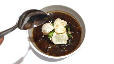 Black meat soup Rawon with leeks and bean sprouts in a white bowl isolated on white backgroundの写真素材