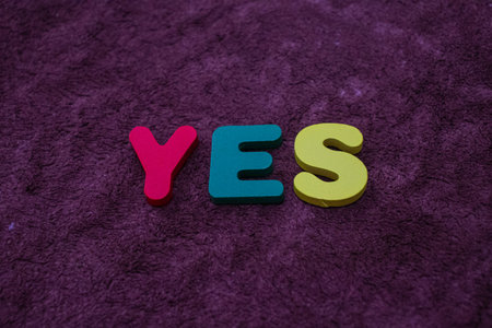 Yes word in colorful wooden letters on a purple background. Business concept