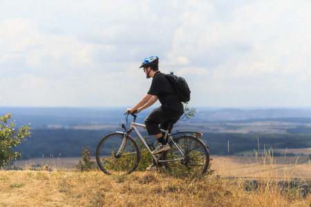 Biking in the Franconian Hills in Northern Bavaria. Caucasian Young man in black sports outfit with...