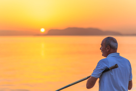 PALERMO, ITALY - SEPTEMBER 19 2015: Italian man with white shirt and white hair fishing in the sunrise on Sicily, Italyのeditorial素材