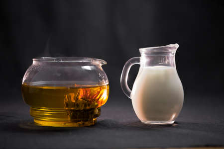 China green blooming tea Bud in a glass teapot. Milk in a small jug on black background