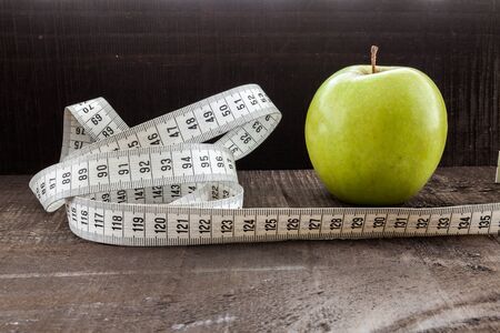 The image shows apple surrounded by a measuring tape Referring to diet and health concept on wooden...