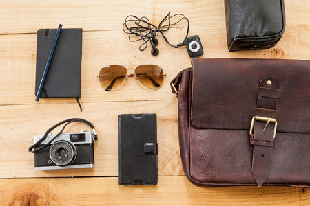 The image shows a retro or hipster bag for man or woman with glasses Such stuff as, vintage camera, leather book bag and a note on a wooden backgroundの写真素材