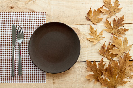 The image shows a wooden table with a plate and cutlery as seasonal rustic decor as backgroundの写真素材