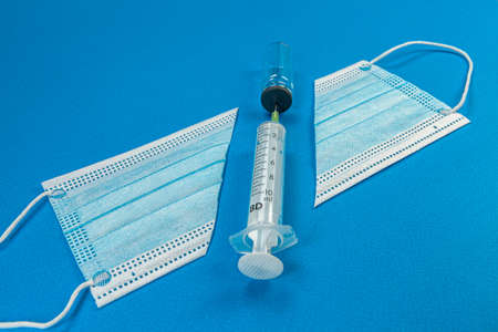 Classic surgical mask on blue background and glass vaccine bottle