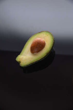 half avocado with pin on black glass. dark avocado on a white background.
