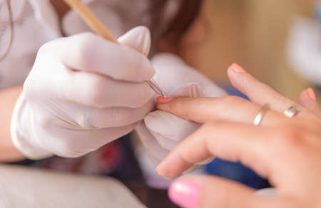 Manicure process in a beauty salon. Close-up of a manicurist hands in white gloves doing manicureの写真素材