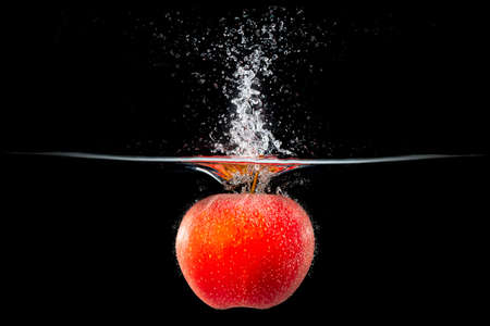 red apple falling into splashing waterの写真素材