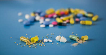 Tablets, pills and capsules on a blurred background that are opened or cut in the middle.