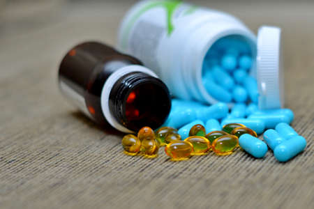 White pills spilling out of a toppled bright red orange pill bottle