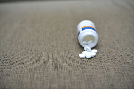 White pills spilling out of a toppled bright red orange pill bottle