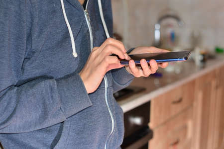 girl with phone in the kitchen. Woman typing write message on smart phone in a modern cafe.