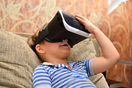 Low angle portrait of little boy wearing VR glasses watching 360 videos and playing augmented...