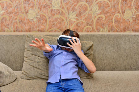 Happy teen boy wearing virtual reality goggles watching movies or playing video games. Cheerful...