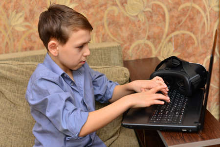 Vertical image of young boy in shirt using laptop computer and sitting on books. Isolated gray backgroundの写真素材