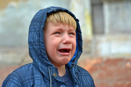 A boy in a blue jacket in a hood, crying with tearsの写真素材