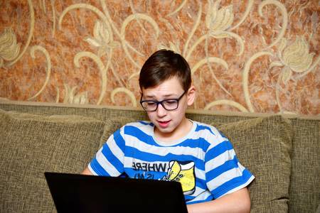 A boy with a laptop in a pinstripe suit is sitting on the couch and looking. He works at the computer.の写真素材