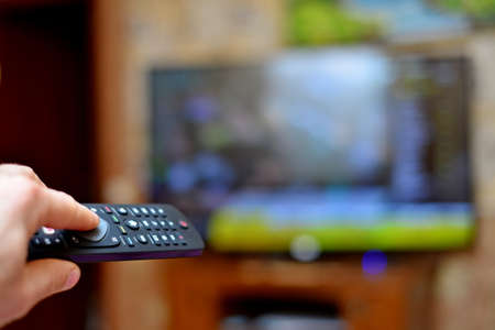 The man switches the news channels on the remote control on TV.