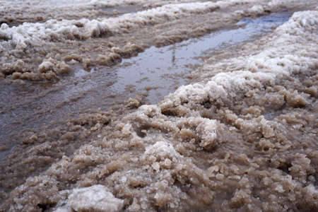 The snow melts on the road and turns into a puddle and slush in the city