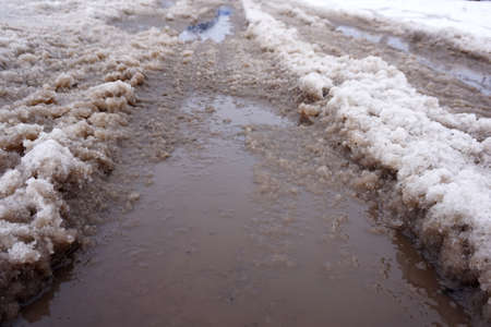 The snow melts on the road and turns into a puddle and slush in the city