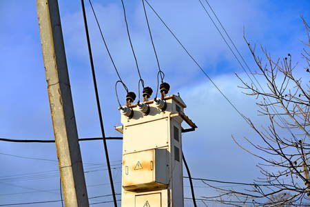 Wooden electric pole with wires on the street in the city against a blue sky.