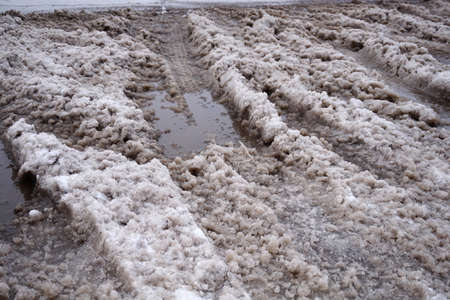 The snow melts on the road and turns into a puddle and slush in the cityの写真素材