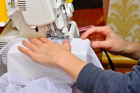A woman sews a white cloth on a sewing machine close-up at the factory. Work seamstress for earnings. Sewing on the sewing machineの写真素材