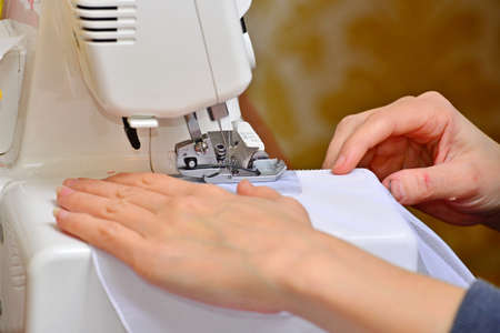 A woman sews a white cloth on a sewing machine close-up at the factory. Work seamstress for...