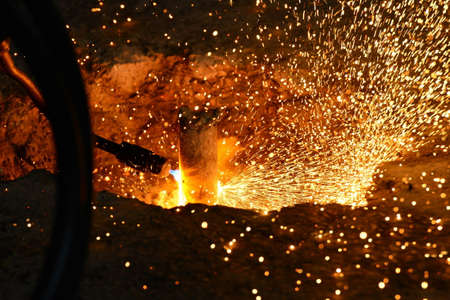 The welder cuts the steel rod using a high-temperature gas cutter. Sparks and drops of molten metal scatter throughout the shop.の写真素材