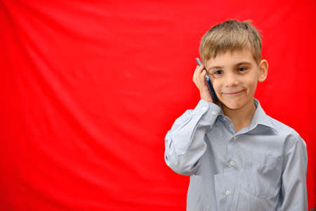 A boy is talking on the phone on a red background in the studioの写真素材
