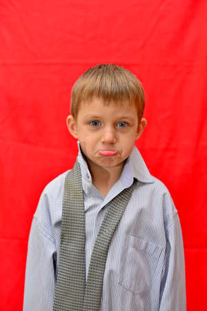 Portrait of a boy in a big shirt on a red background in the studio