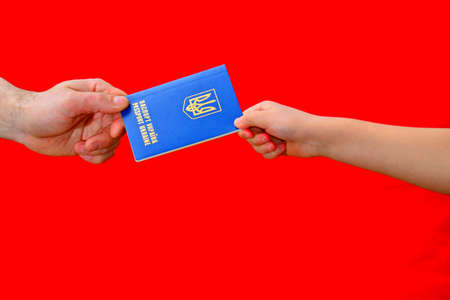 A man passes the passport of ukraine on a red background, hands accepting a document.の写真素材