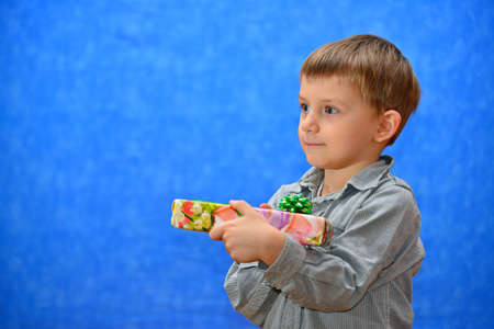 A boy with a gift in his hands in the studio on a blue background look into the distanceの写真素材