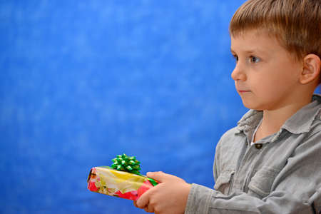 A boy with a gift in his hands in the studio on a blue background look into the distanceの写真素材