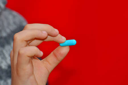 A girl holds a blue tablet with two fingers. Blue capsules in hand, medicine for health.の写真素材