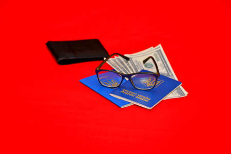 Two Ukrainian passports with glasses, a black purse and dollars on an isolated red background. The concept of traveling alone, in love.の写真素材
