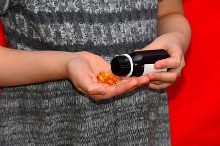 The girl takes out the yellow tablets from the jar. The concept of business, health and prosperity.の写真素材