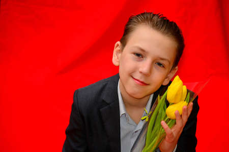 Boy in a suit with tulips on a red background. Photo portrait in the studio.の写真素材