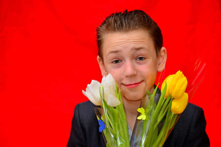 Boy in a suit with tulips on a red background. Photo portrait in the studio.の写真素材