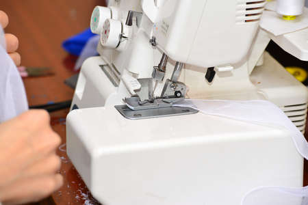 The woman at the sewing machine processes a white fabric, on manufacture close-up of a hand.の写真素材
