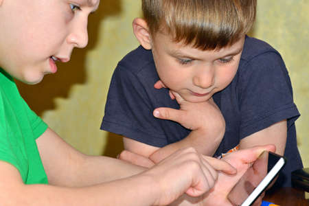 Children two brothers play on the smartphone in the game. One looks like the other is typing on the keyboard on the phone.の写真素材