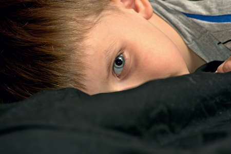 The boy on the black bed prepares for bed and looks at you in the bedroom.
