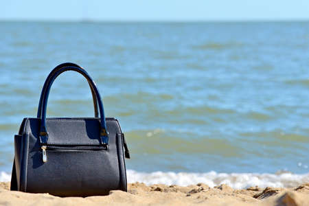 Black bag on the beach on a background of blue sea, ocean. The concept of leisure and vacation.の写真素材