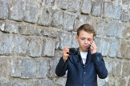 A boy with a camera is writing a message on a smartphone, on the street