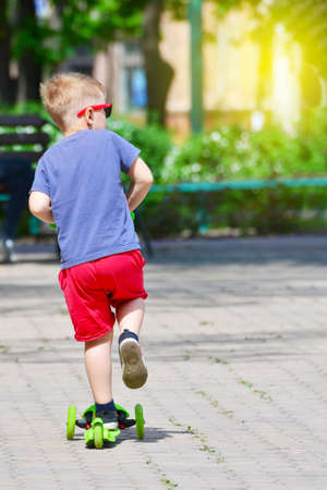 The boy skates on a scooter in the summer in the park, outdoor activities and outdoor sports for children.の写真素材