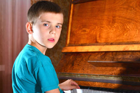 The boy plays the guitar near the piano and looks thoughtfullyの写真素材
