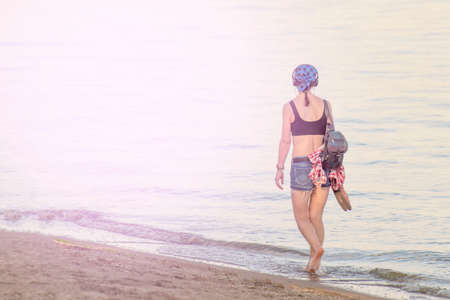 The girl walks along the ocean shore in clothes and looks ahead, the concept of an unknown future.