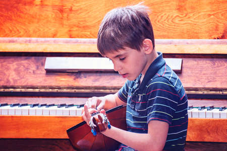 The boy plays the guitar and takes chords, dombra on the background of the piano.の写真素材