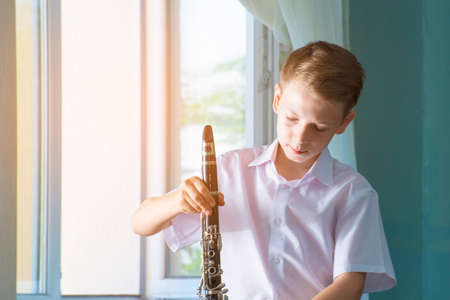 The boy is standing by the window with a black clarinet. Musicology, music education and educationの写真素材